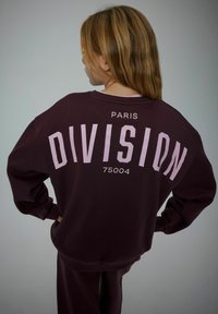 Bordo oversized dukserica s natpisom "PARIS DIVISION 75004" u ružičastim slovima na leđima. Mekani materijal s opuštenim krojem i rebrastim manžetama.