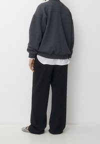 Oversized donkergrijs sweatshirt en zwarte wijde broek, gelaagd over een wit shirt. Grijze platte schoenen met een textuur. Eenvoudig en casual ontwerp.