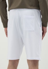 Pantaloni corti bianchi in cotone con una tasca posteriore, vestibilità rilassata e una texture liscia. La vita è elastica e l'orlo è cucito con cura.