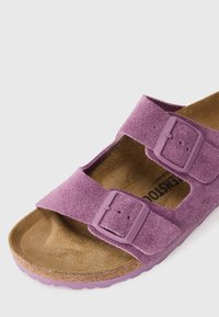 Purple suede sandal with two adjustable straps featuring buckles, a cork footbed, and a textured rubber sole.