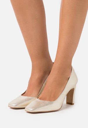 Chaussures à talons hauts métalliques dorées avec un bout carré, une texture lisse, et un talon bloc de soutien, présentant un design simple et élégant.