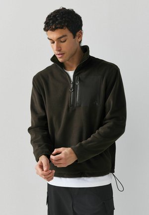 Brown fleece pullover with a quarter zip and a chest pocket, featuring adjustable hem, long sleeves, and a soft texture.
