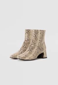 Bottines en cuir de serpent beige avec une surface texturée, un bout pointu et un talon épais. Design élégant et minimaliste.