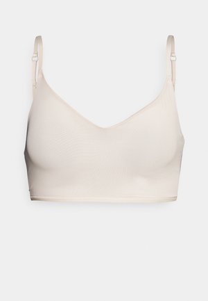 Beige seamless bra with a v-neck design, adjustable straps, and soft texture. No underwire, smooth edges, and minimal stitching details.