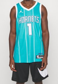 Tummanvihreä koripallopaita, jossa on valkoisia yksityiskohtia, ja se näyttää "HORNETS"-tekstin sekä pelaajan numeron 1. Valmistettu verkkomateriaalista, jossa on pystysuorat raidat.