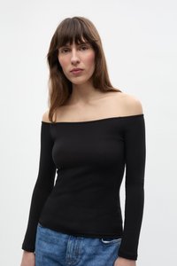 Juodas off-the-shoulder ilgomis rankovėmis topas su prigludusia forma ir lygiu tekstūra, derinamas su šviesiai mėlynomis džinsinėmis kelnėmis.