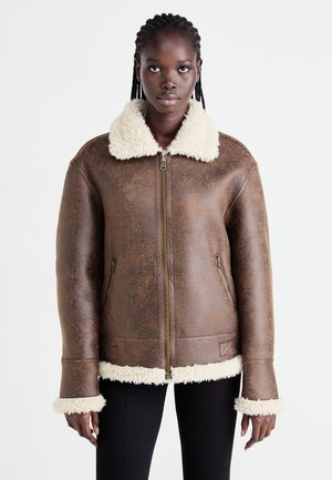 Braune, strukturiert Lederjacke mit einem Kragen und Manschetten aus cremefarbenem Kunstfell, ausgestattet mit einem Reißverschluss vorne und zwei seitlichen Taschen.