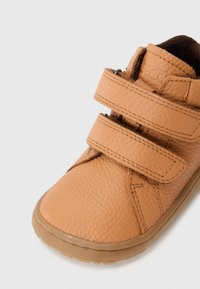 Tan leren schoen met twee verstelbare klittenbandbanden, tekstuur oppervlak, ronde teen en rubberen zool voor grip en comfort.