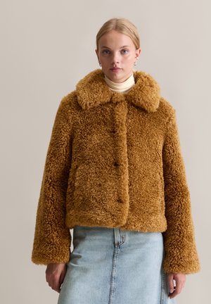 Bruine nepbontjas met een grote kraag, knoopsluiting en brede mouwen. Draag boven een lichte coltrui en denimrok. Zachte textuur.