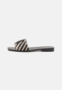 Sandali piatti a strisce con tomaia intrecciata in nero e beige, caratterizzati da una suola nera liscia e un design minimalista. Senza tacco, con punta aperta.
