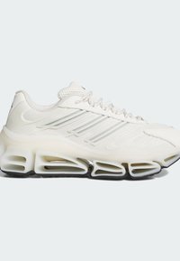 Baskets de sport blanches avec empeigne en mesh, fermeture à lacets sur le devant, trois bandes réfléchissantes sur le côté et une semelle épaisse segmentée avec une semelle noire.