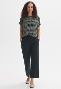 Top a righe bianco e nero con maniche corte, abbinato a pantaloni larghi verde scuro e scarpe basse beige chiaro.
