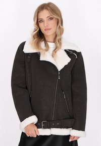 Dunkelbraune Schaffelljacke mit einem weißen flauschigen Kragen, Reißverschluss vorne, Seitentaschen und einer Taillierung mit einem Gürtel und einer Metall-Schnalle.