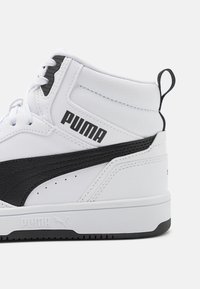 Baskets montantes blanches avec des accents noirs, cuir texturé, logo bien visible, design à lacets et une languette à l'arrière du talon.