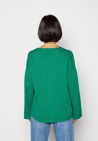 Groene, lange mouwen pullover trui met een ronde halslijn en een casual pasvorm. Zachte textuur met een gladde afwerking. Blauwe jeans eronder gedragen.