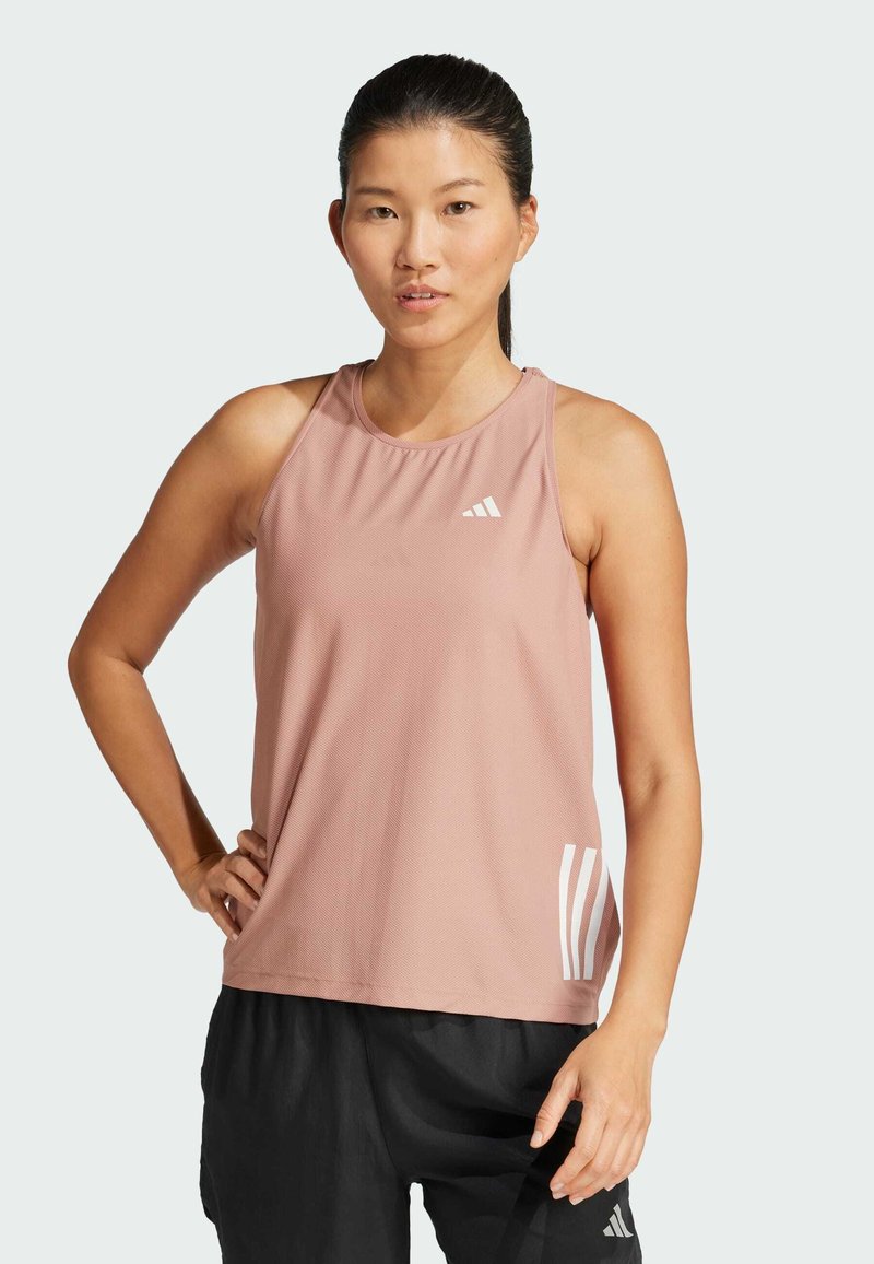 Lichtroze sporttanktop met een textuurstof, voorzien van het witte Adidas-logo en drie strokenaccenten aan de zijkant. Zwarte shorts.