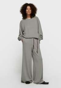 Sweat-shirt gris et pantalon à jambes larges en tissu doux avec un design texturé, doté d'un cordon de serrage et de poches latérales, porté avec des chaussures noires.