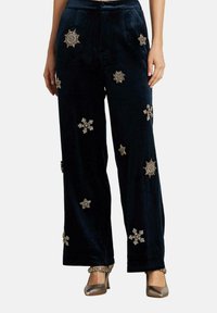 Pantalones de terciopelo azul marino con corte de pierna ancha, adornados con patrones de estrellas y copos de nieve en tono dorado, con una textura suave y un corte a la altura del tobillo.