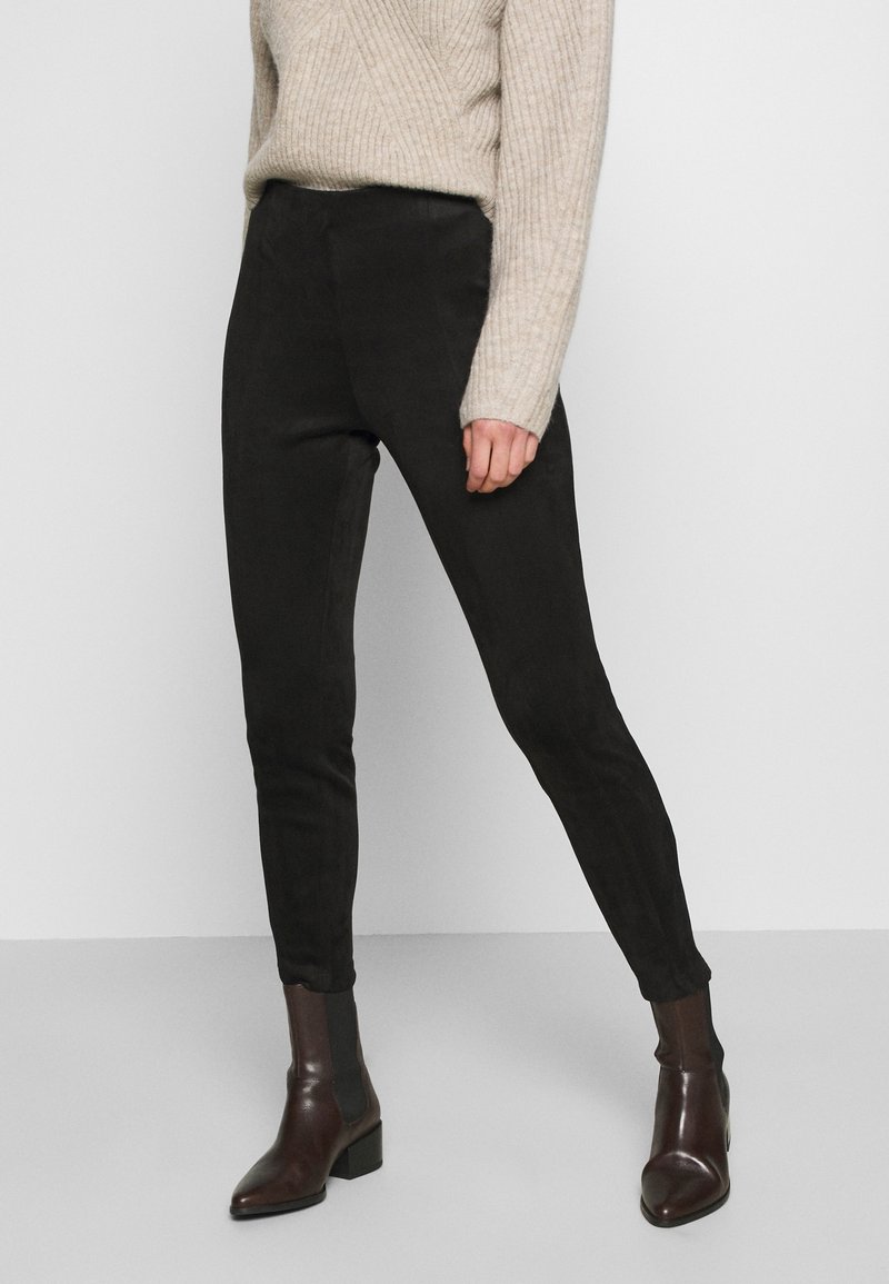 Czarne, dopasowane spodnie wykonane z miękkiego materiału o gładkiej fakturze, w zestawieniu z brązowymi botkami za kostkę. Spodnie mają wysoki stan.