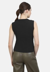 Zwarte mouwloze top met een aansluitend ontwerp, geribbelde textuur en een hoge halslijn, gecombineerd met olijfgroene leren broek.