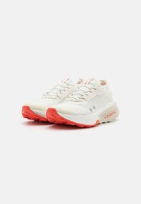 Sportliche Schuhe mit einem leichten weißen Mesh-Obermaterial, roten Akzenten an der Sohle und den Ösen sowie einer gepolsterten Sohle für zusätzlichen Komfort.