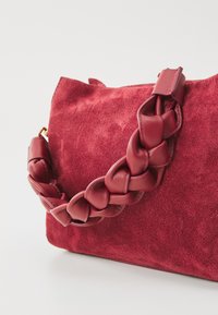 Red suede bag with a braided leather strap. Features a soft texture, slouchy design, and a gold-toned hardware accent.