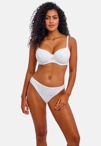 Ensemble de lingerie blanche comprenant un motif géométrique texturé, un soutien-gorge moulé avec bretelles réglables et des culottes bikini taille haute assorties.