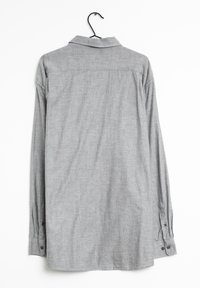 Chemise grise à manches longues avec col boutonné, texture subtile et poignets à deux boutons, présentée sur un cintre.