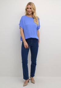 Top corto a maniche corte dal taglio morbido in un vivace blu, abbinato a jeans skinny blu scuro e décolleté beige a punta. Design semplice e pulito.