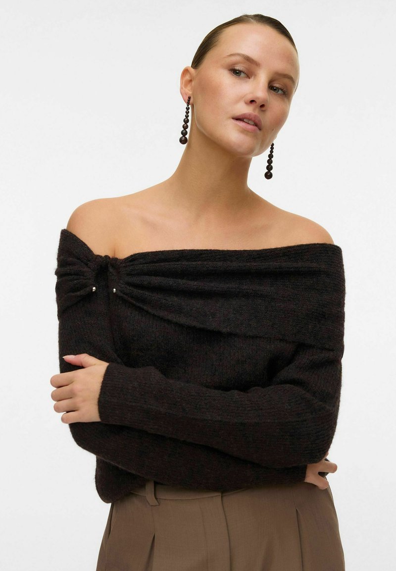 Off-shoulder svart stickad tröja med en texturerad finish, med en vriden detalj vid halslinningen och små metallicdetaljer.