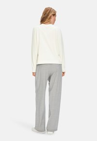 Helle beige Pullover mit einem V-förmigen Rückenpasse, kombiniert mit grauen, karierten Weitbein-Hosen und weißen Sneakern, die eine glatte Textur aufweisen.