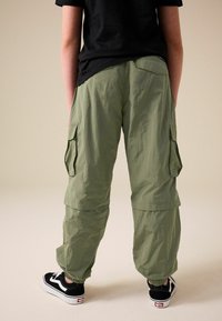 Pantaloni cargo in verde oliva chiaro, con cintura elastica, molteplici tasche laterali e una vestibilità rilassata. Abbinati a sneaker nere.