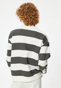 Sweatshirt a righe grigie e bianche con collo tondo, spalle cadenti e polsini a costine, realizzato in un materiale morbido e elasticizzato.