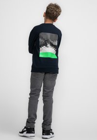 Marine sweatshirt met een bergafbeelding in zwart-wit, met een groene accent. Gecombineerd met grijze jeans en zwarte sneakers.