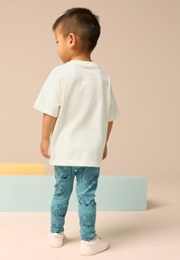 Light-colored, short-sleeve t-shirt paired with teal leggings featuring a cartoon dog pattern. White sneakers complete the outfit.