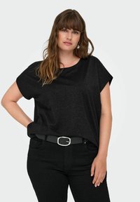 Svart kortärmad topp med rundad halsringning, tillverkad av strukturerad tyg. Bärs med svarta jeans och ett enkelt bälte med en silverspänne.