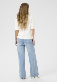 Lichtgekleurde, gestructureerde gebreide top met korte mouwen, gecombineerd met loszittende, lichtblauwe denim jeans en witte open-teen hakken.