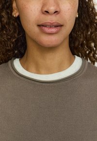 Pruun soonik, mille all on valge ümar kaelus. Kerges tekstuuris kangas, ümar kaelus ja lihtne disain.