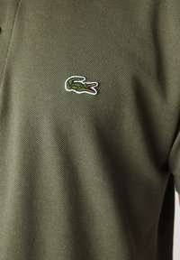 Zelená polo košeľa so štruktúrovanou textíliou, s malým vyšitým logom krokodíla v zelenej a červenej farbe na ľavej strane hrudníka.