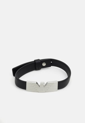 Black leather bracelet with a metal clasp featuring a striped eagle design and engraved logo. Adjustable fit with a snap closure.