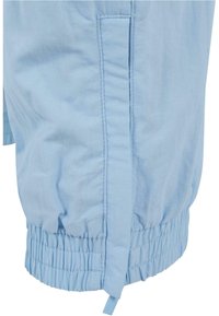 Light blue, lightweight jacket fabric, featuring gathered elastic at the hem, vertical seam details, and a side tie for adjustable fit.