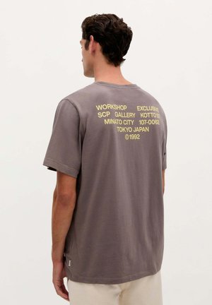 Gray cotton t-shirt with short sleeves, featuring yellow text on the back, including location and year details. Soft texture and relaxed fit.