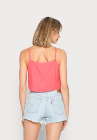 Top cropped rosa com alças ajustáveis, combinado com calções de denim azul claro com margens desfiadas e bolsos traseiros.