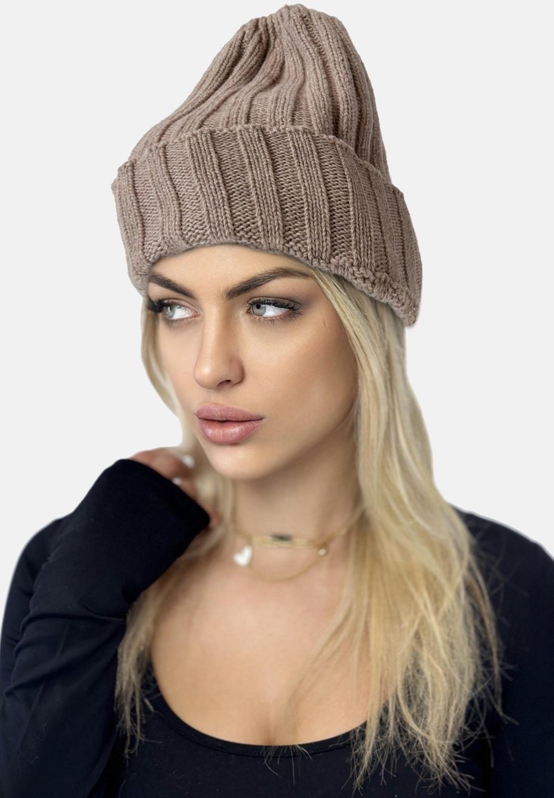 Gorro de punto beig con textura acanalada, que presenta un puño alto y doblado. Llevado con una camiseta de manga larga negra. Fondo liso.
