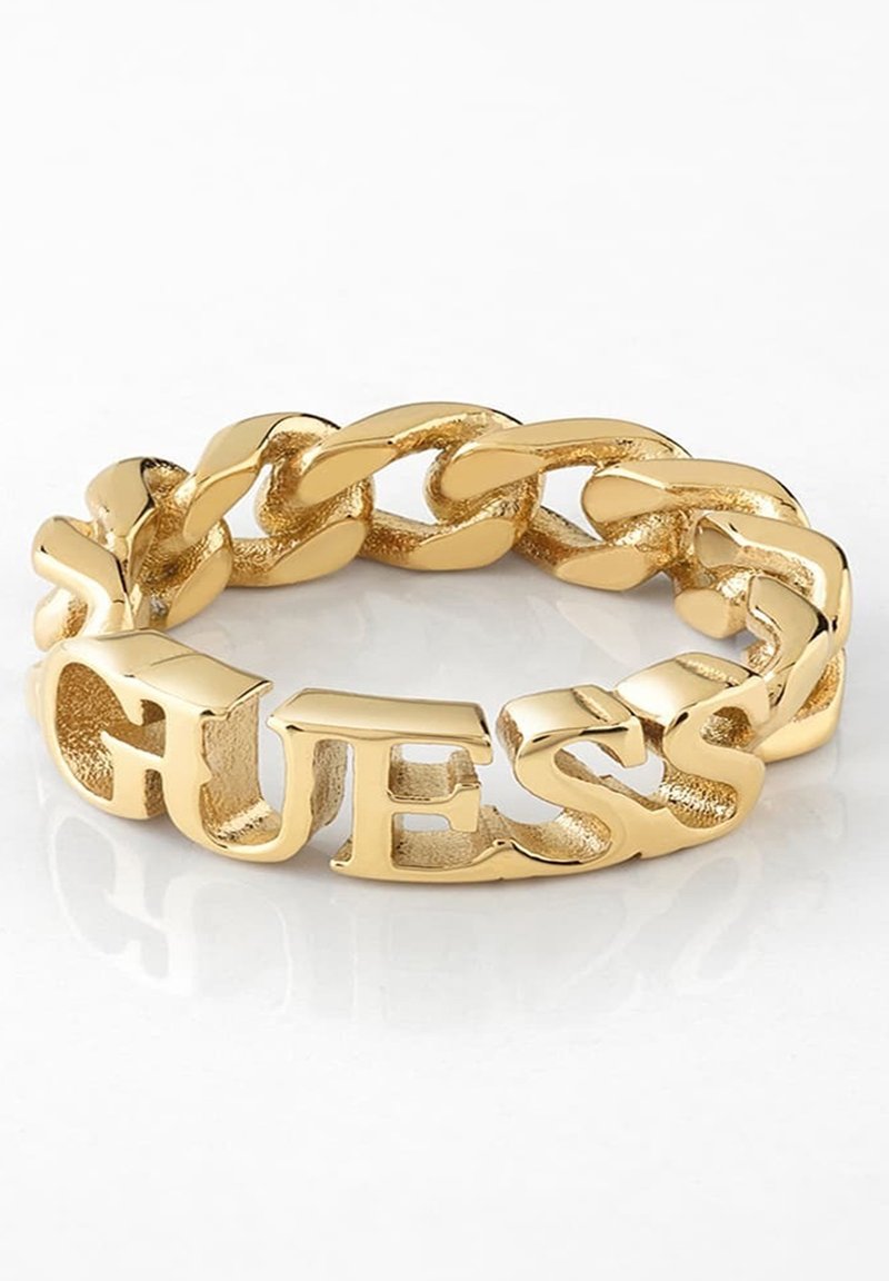 Bracelet chaîne en or avec de gros maillons et le mot "GUESS" intégré de manière visible dans le design sur une surface blanche.