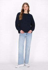 Felpa oversize blu navy con collo rotondo, abbinata a jeans azzurri a gamba larga e sneakers bianche. Tessuto morbido, design casual.