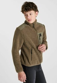Bruine fleece jack met een ritssluiting aan de voorkant, hoge kraag en olijfgroene schouderaccenten. Heeft twee ritszakken voor opslag.
