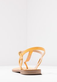 Gule lædersandaler med flad sål, der har en spænde-strop og et åbent design. Indersålen er struktureret for at give et godt greb.