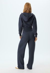 Felpa cropped blu navy con cappuccio e polsini, abbinata a pantaloni della tuta larghi coordinati. Tessuto morbido con vita elastica, design minimale.