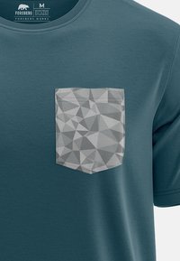 Camiseta de algodón verde azulado con un bolsillo de patrón geométrico gris, escote redondo y mangas cortas. Textura suave y diseño sencillo.